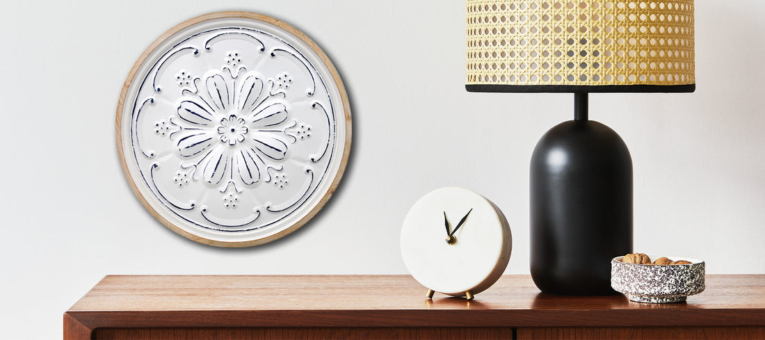 Wood cabinet with a lamp, clock on it and wall medallion hanging above the cabinet.
