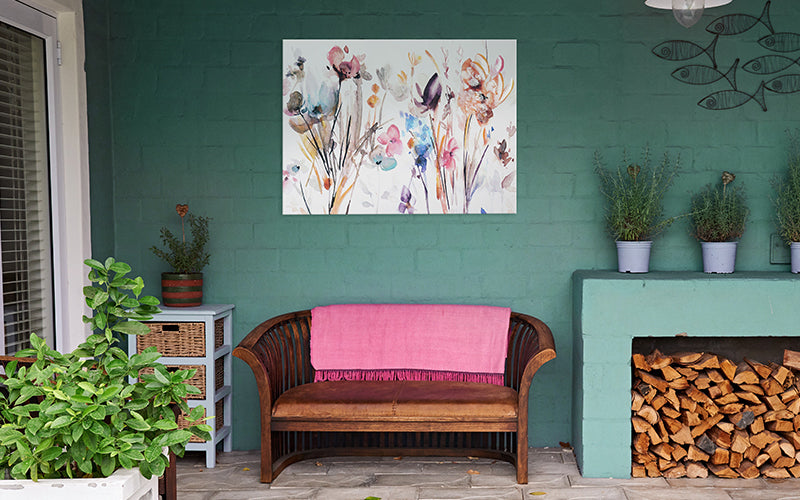 Watercolor Plum & Earth Flowers Embellished Canvas Art Print hanging on a turquoise patio wall above a wood love seat and plants. 