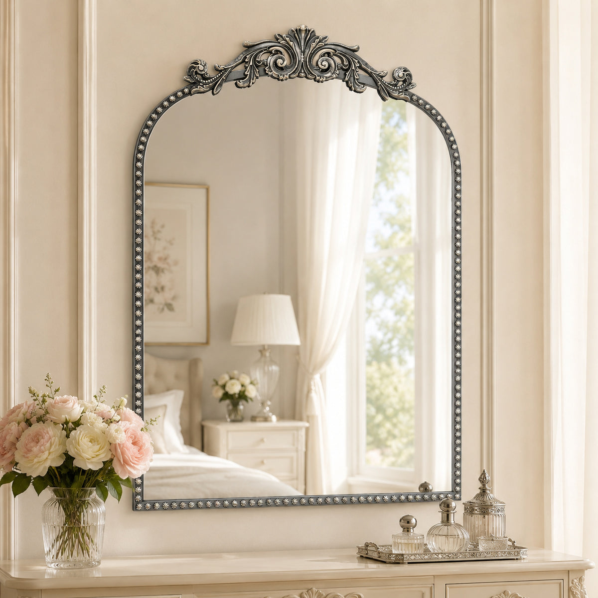 A 20 x 30 pewter arched vanity mirror with antique silver filigree crest and beaded edge, mounted vertically above a compact dresser in a bright neutral room.