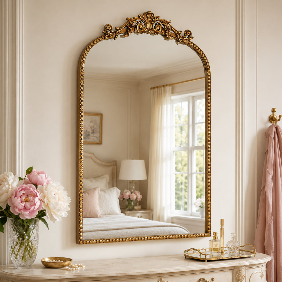 A compact 20 x 30 antique gold arched wall mirror with filigree crest and beaded trim, displayed vertically above a vanity for grooming in a warm dressing space.