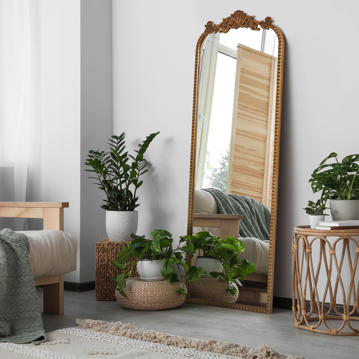 A slim 22 x 64 antique gold arched full body mirror with ornate filigree crest and floral-bead border, leaning beside a dresser and closet in a warm bedroom.